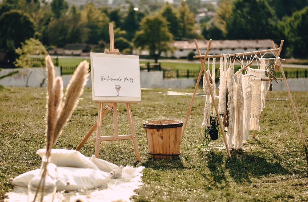 A Boho-themed Bachelorette Party with a Sign, Makeshift Clothes Railing, and Wooden Bucket